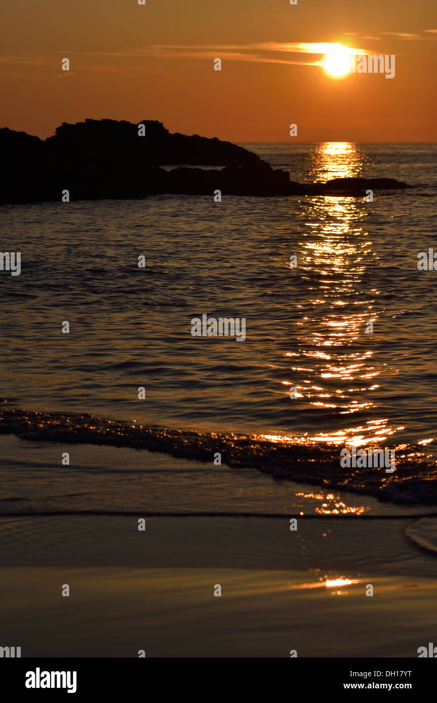 Bild von einem Sonnenuntergang Strand mit Felsen im Hintergrund abhebt. Stockfoto