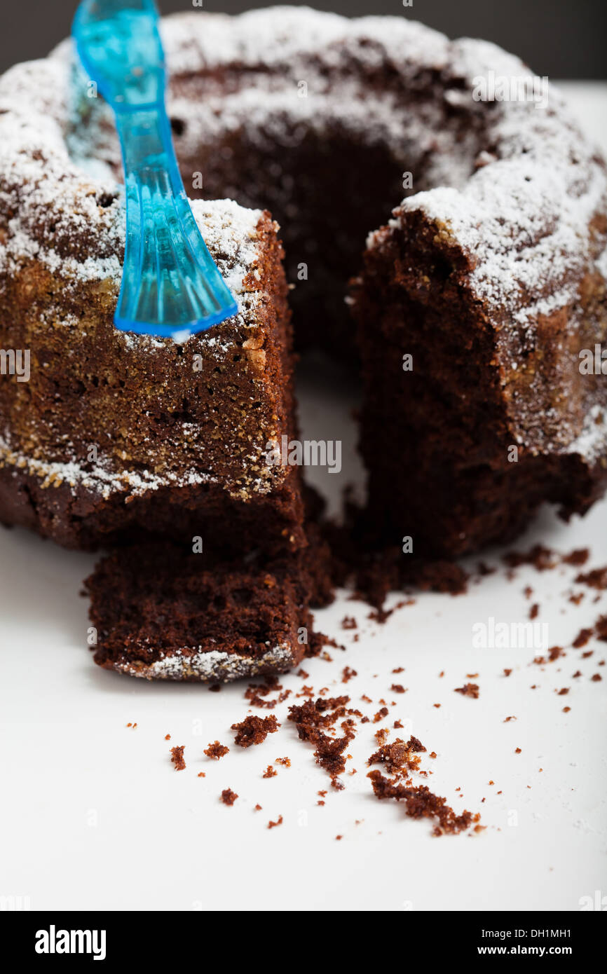 Nahaufnahme des trockenen Schokoladenkuchen mit Stück Ausschneiden bestreut mit Puderzucker und blauen Kunststoff-Gabel Stockfoto