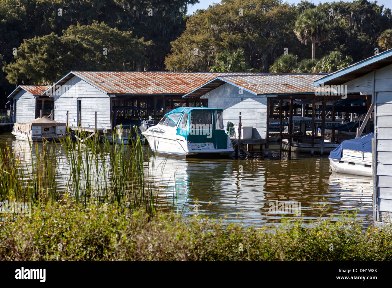 Boote und Motoryacht mit türkisfarbenen Baldachin vor Anker von Bootshäusern, See Dora, Mount Dora, Florida USA Stockfoto