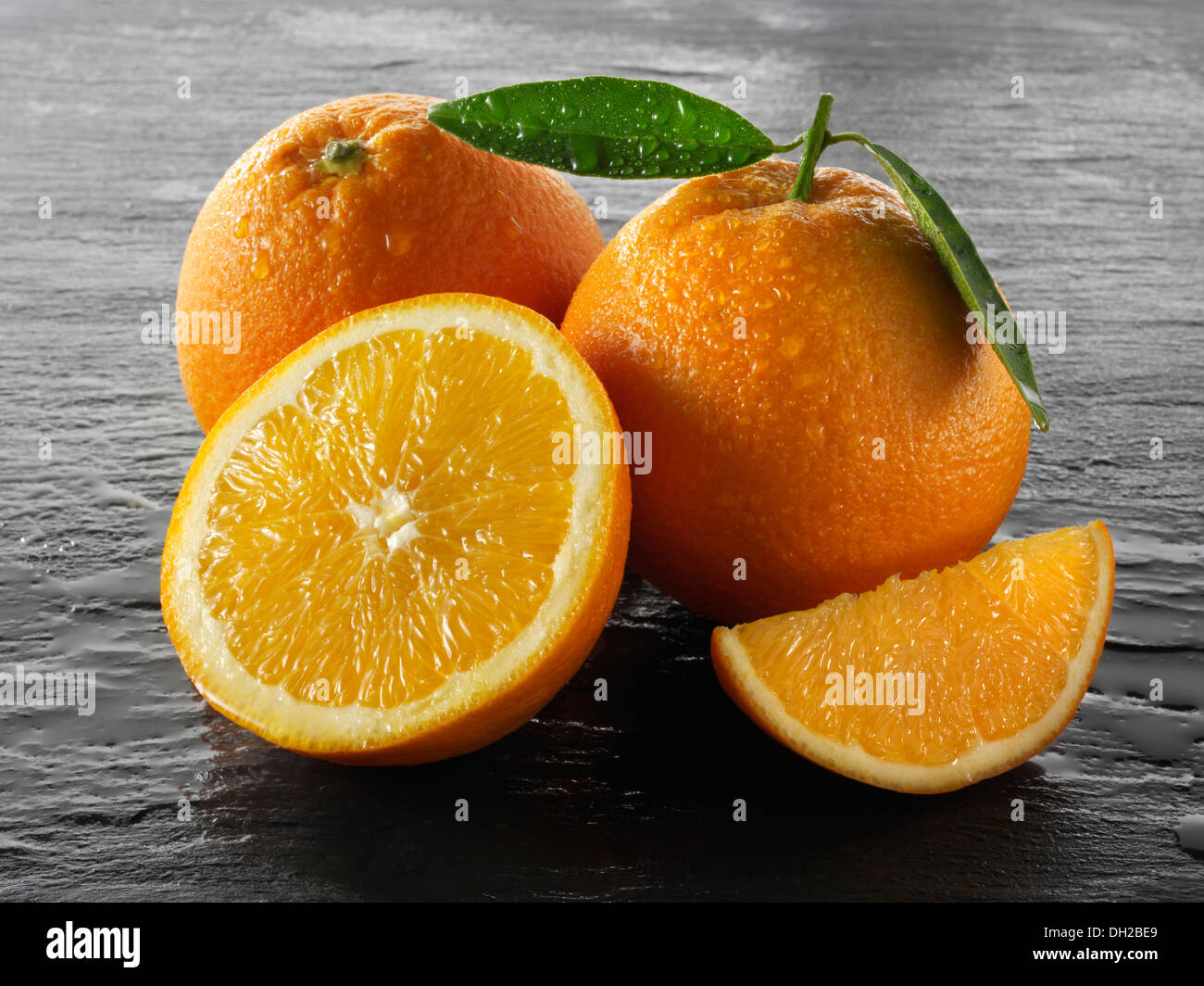 Ganze und geschnittene frische Orangen mit Blättern Stockfoto