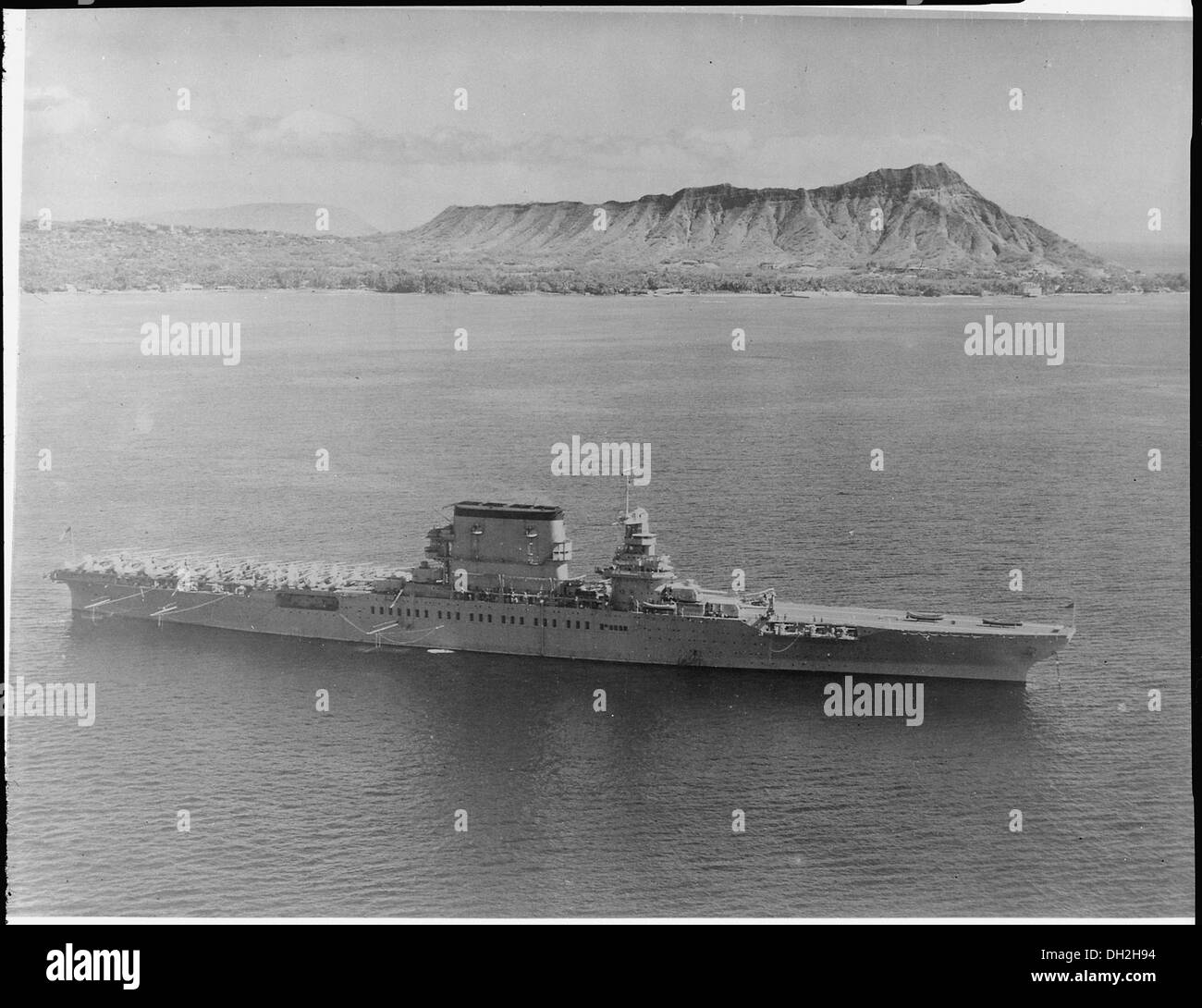 Eine Luftaufnahme der USS Lexington (CV-2) mit Flugzeugen an Deck, mit einem Steuerbordbalken mit Diamond Head im Hintergrund, was die Präsenz des Schiffes auf der Marine unterstreicht. Stockfoto