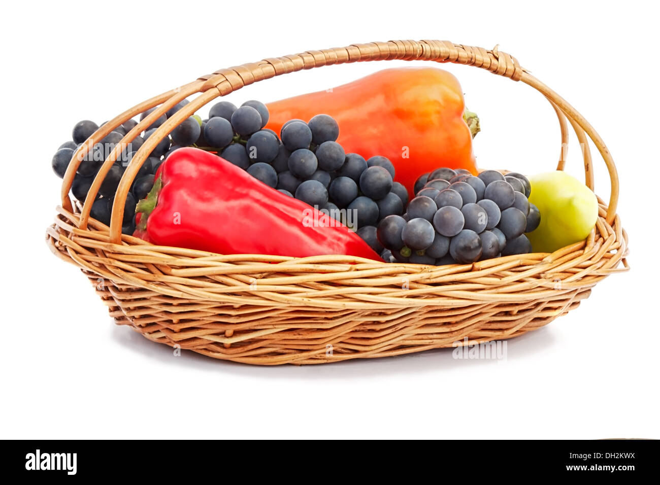 Die reifen Früchte der Trauben in einem Weidenkorb, Paprika rot und gelb. Auf weißem Hintergrund dargestellt. Stockfoto