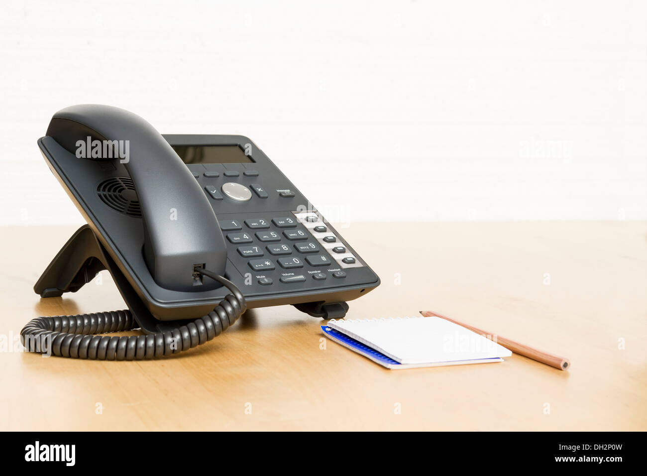 Telefon am Schreibtisch mit Notepad in weißem Hintergrund. Schreibtisch aus Holz. Stockfoto