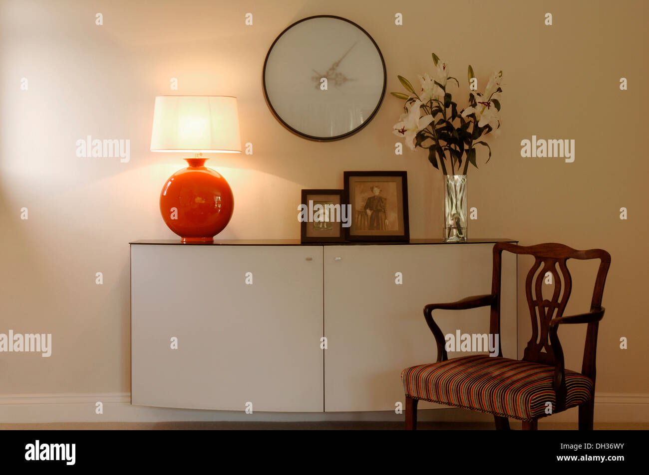 Detail aus einem Wohnzimmer mit Designer Sideboard oder Kabinett Familie fotografiert eine große Wanduhr, Vase mit Blumen Carver Stuhl Stockfoto