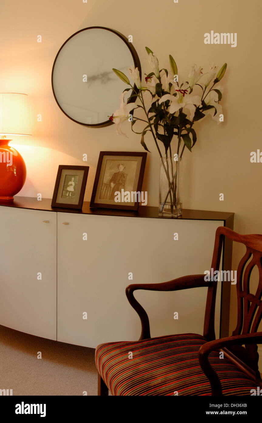 Detail aus einem Wohnzimmer mit Designer Sideboard oder Kabinett Familie fotografiert eine große Wanduhr, Vase mit Blumen Carver Stuhl Stockfoto