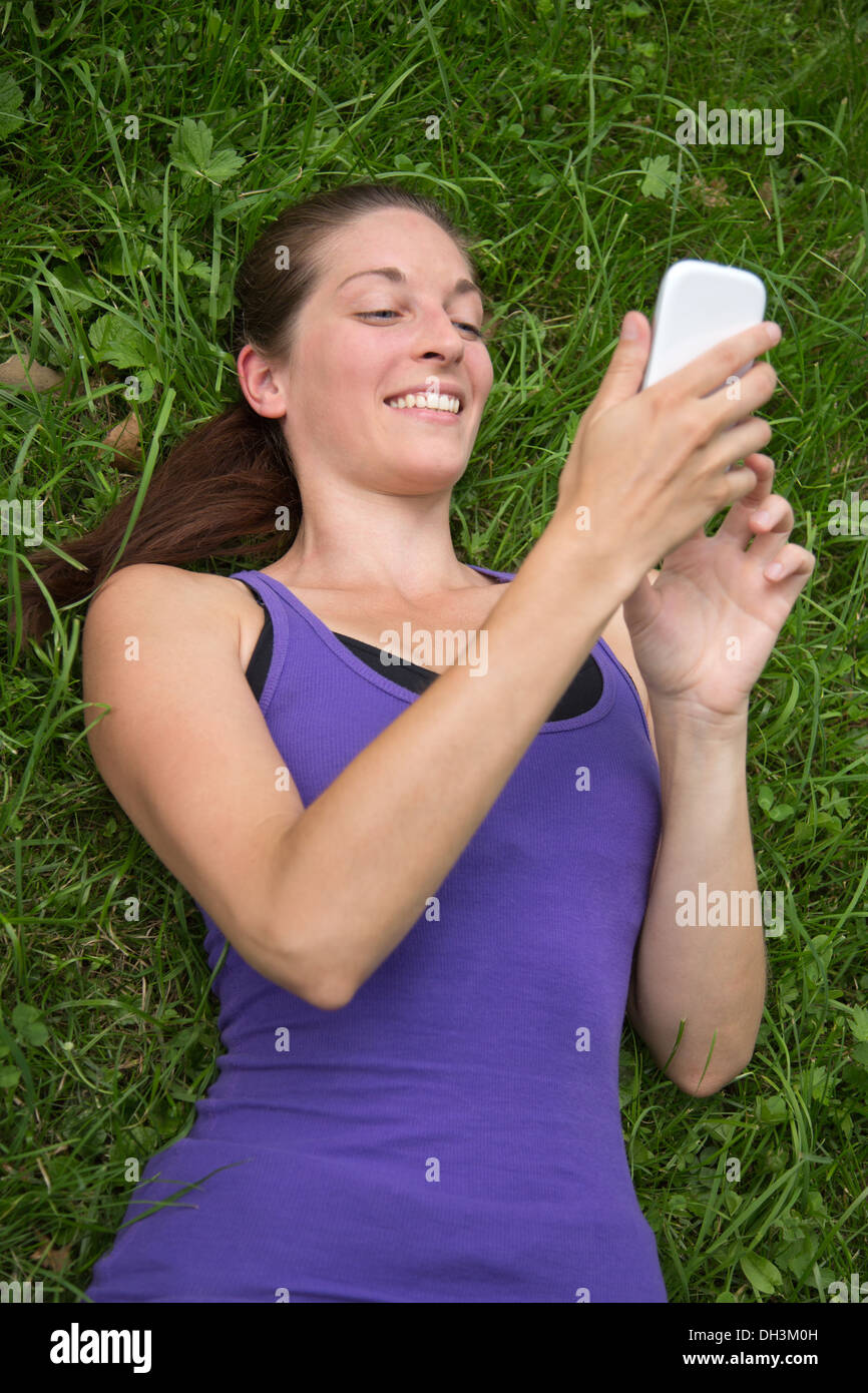 Junge glückliche Frau liegend auf einer grünen Wiese ist ein Smartphone verwenden. Stockfoto