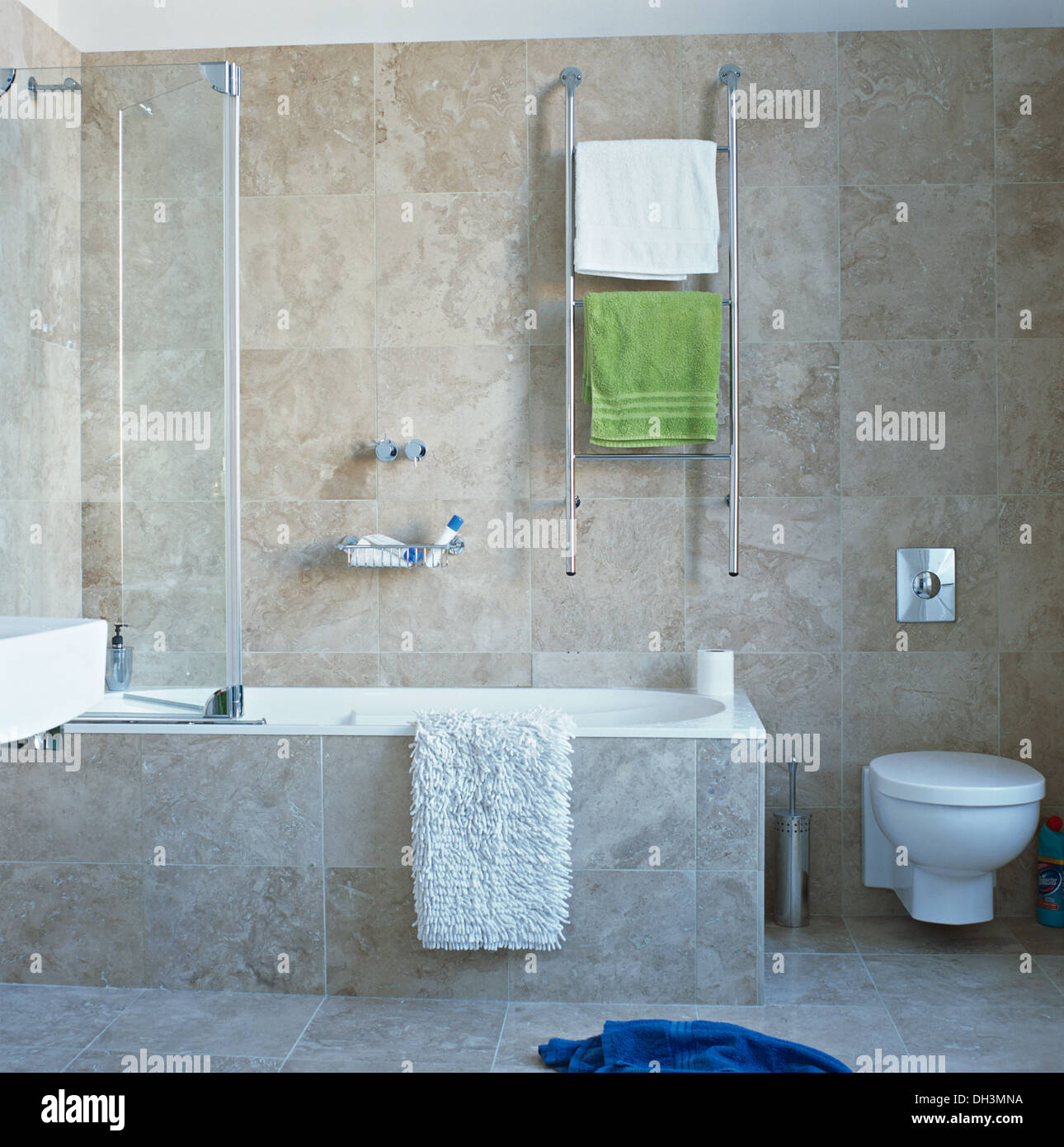 Handtücher auf beheizten Chrom Schiene auf Wand über Bad mit Glas-Dusche Bildschirm und weiß Badematte in modernen grauen gefliestes Badezimmer Stockfotografie