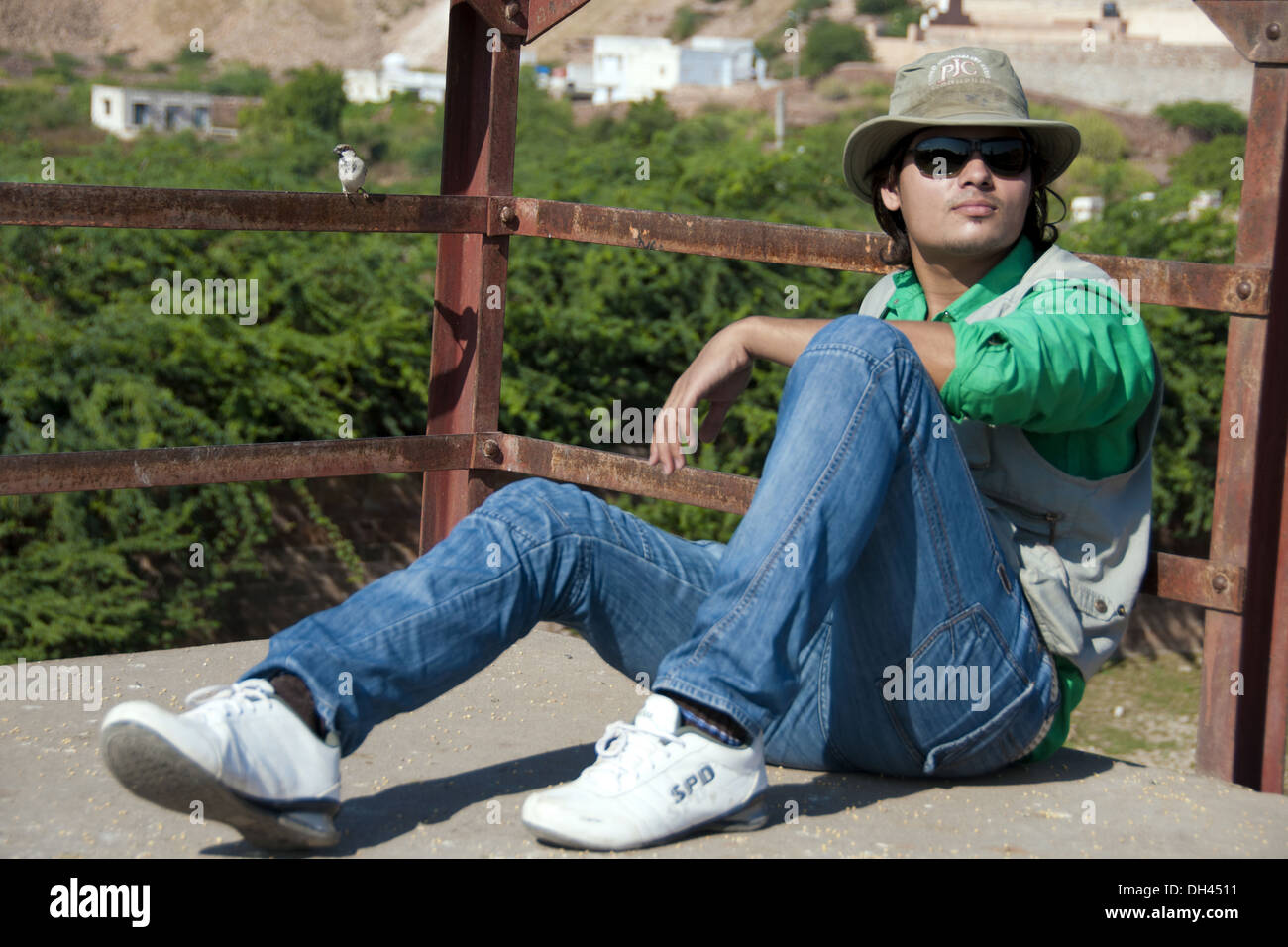 Mann, sitzend blaue Jeans weiße Schuhe grünes Hemd Weste Hut schwarz Sonnenbrille Herr #786 Stockfoto