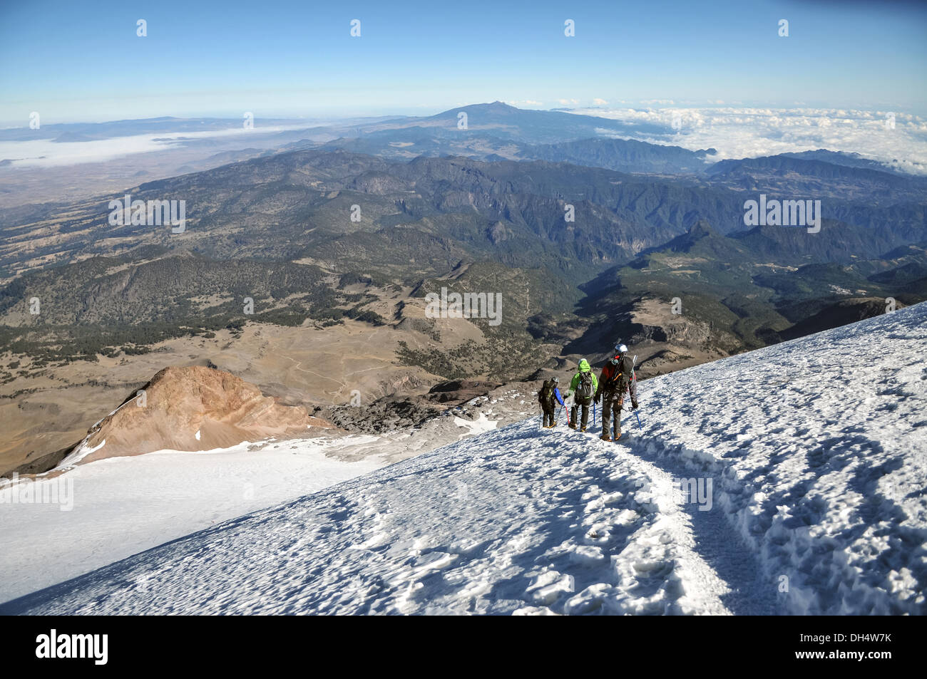 Alpine Bergsteiger steigen einen Gletscher mit Blick auf ein Panorama der Berge und Wolken. Stockfoto