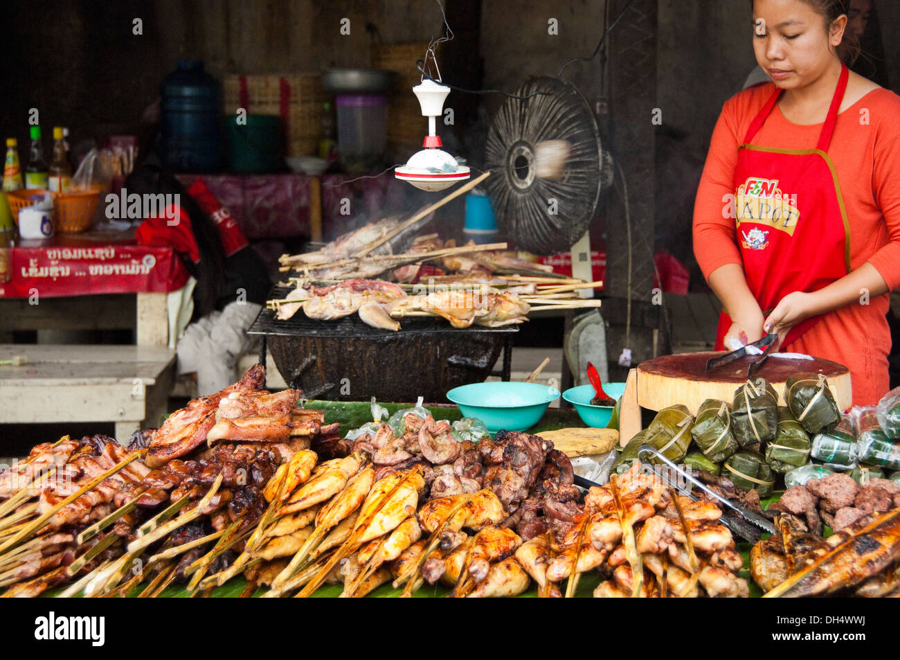 Horizontales Porträt einer Laodame in einem Restaurant am Straßenrand, das in Laos viel Fleisch vom Grill verkauft. Stockfoto