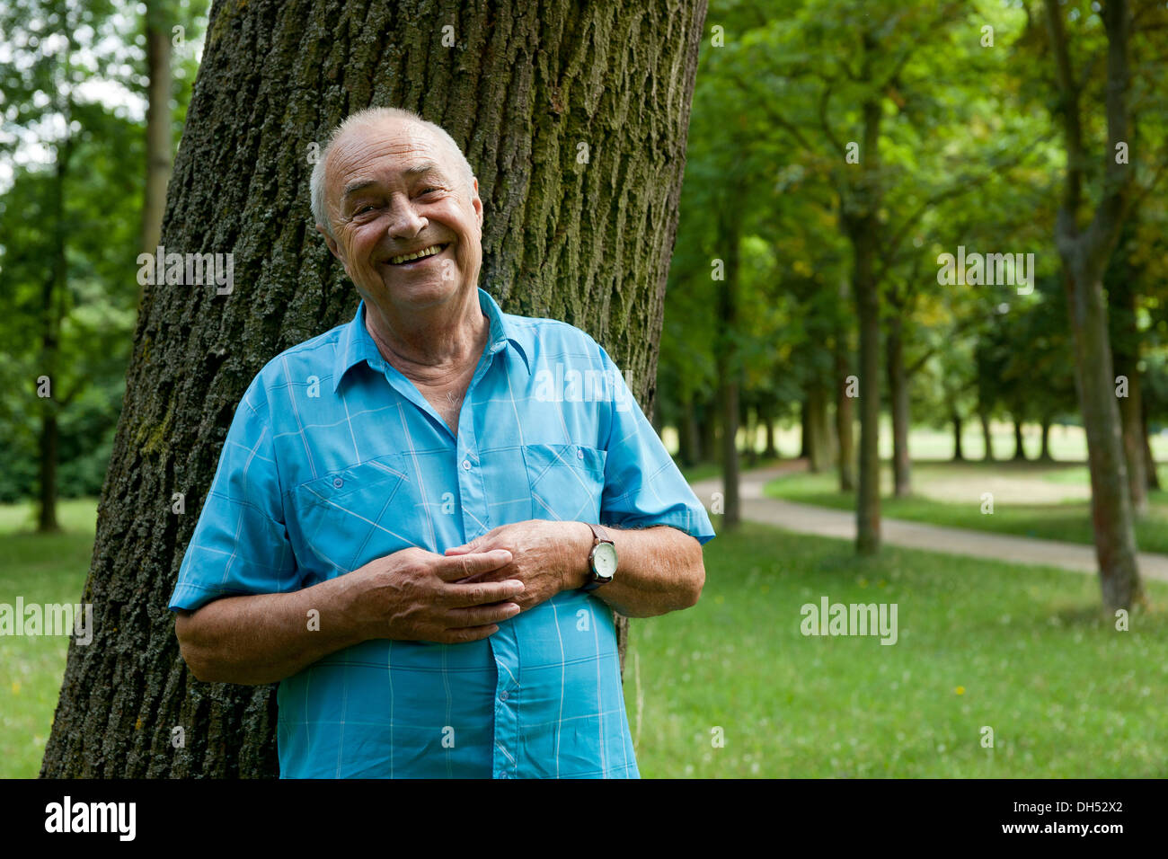 Älterer Mann lehnte sich gegen einen Baum, in einer guten Stimmung Stockfoto