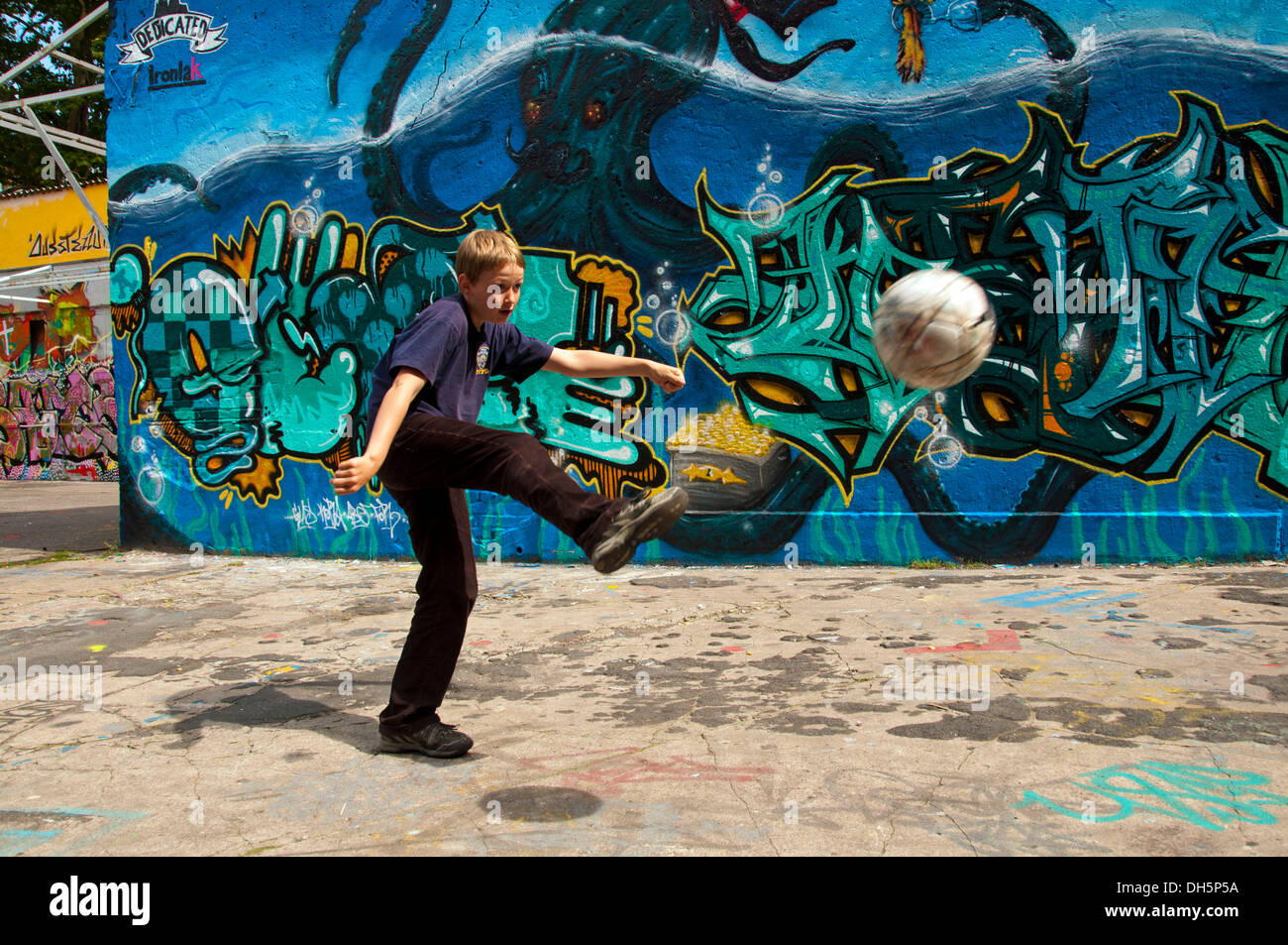 Ein Junge spielt 10 Jahre mit seinem Fußball vor einer Graffitiwand bedeckt, Fußballplatz, Köln Stockfoto