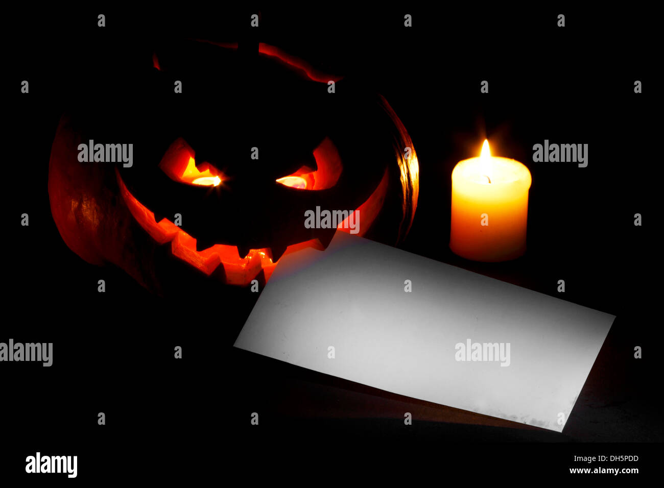 Halloween-Kürbis mit brennender Kerze und Postkarte auf schwarzem Hintergrund Stockfoto