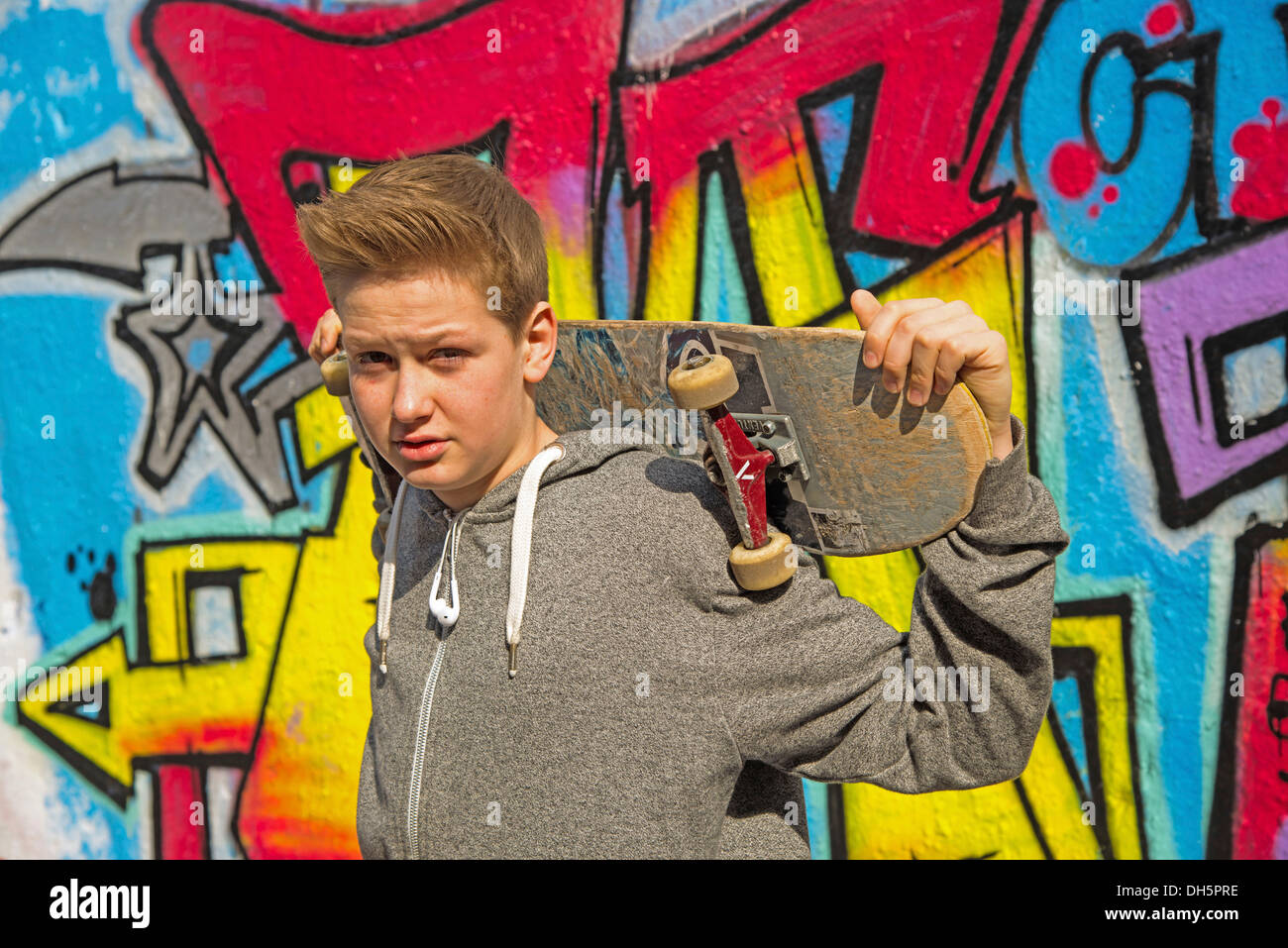 Junge, 13 Jahre, hält eine Skateboard vor Graffiti bewachsenen Wand, Deutschland Stockfoto
