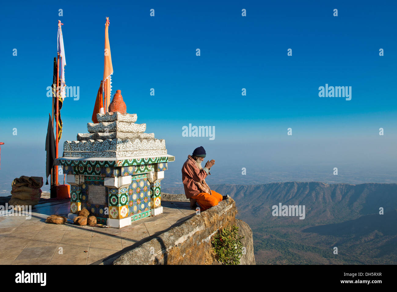 Sadhu oder heiliger Mann sitzt mit seinen Händen gefaltet im Gebet auf den Abgrund vor einem Hindu-Tempel Schrein mit Gebetsfahnen Stockfoto