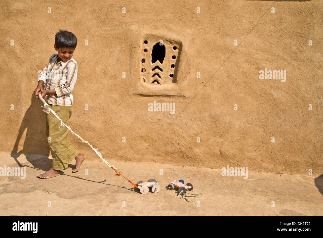 Junge spielt mit einem selbst gebastelten Spielzeugautos außerhalb ein Lehmhaus, Wüste Thar, Rajasthan, Indien Stockfoto