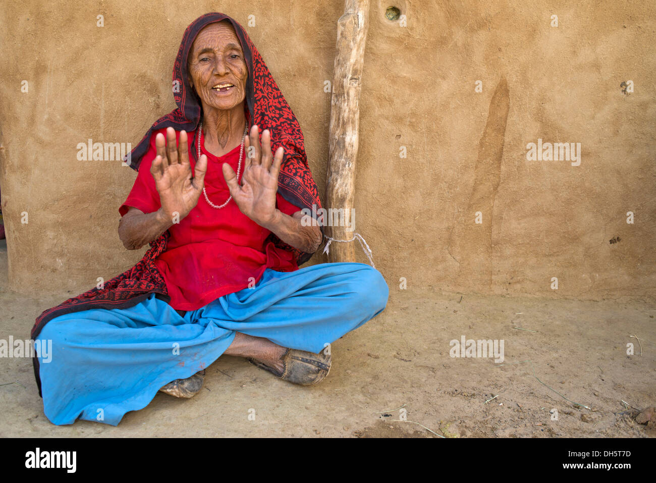 Alte Frau sitzt auf dem Boden vor ihrem Haus gestikulierend, Wüste Thar, Rajasthan, Indien Stockfoto