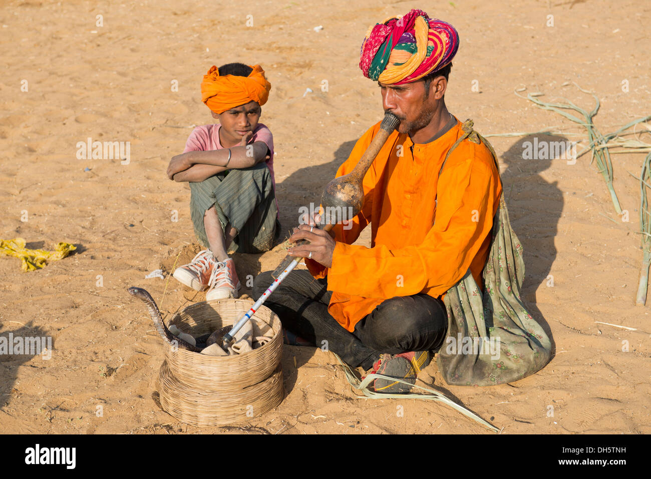 Rajasthani Schlangenbeschwörer mit einem Turban, eine Querflöte, eine Kobra oder Naja Wicklung aus einem Korb vor ihm zu spielen Stockfoto