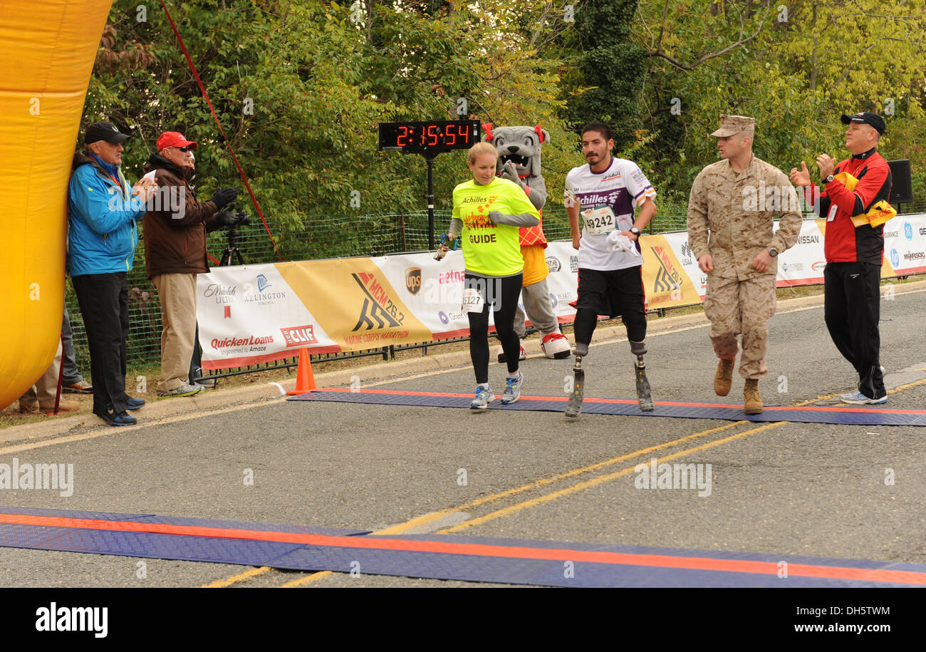 Ein Teilnehmer überquert die Ziellinie beim 38. jährlichen Marine Corps Marathon als Unterstützer und Veranstaltung Freiwilligen jubeln ihm auf. Stockfoto