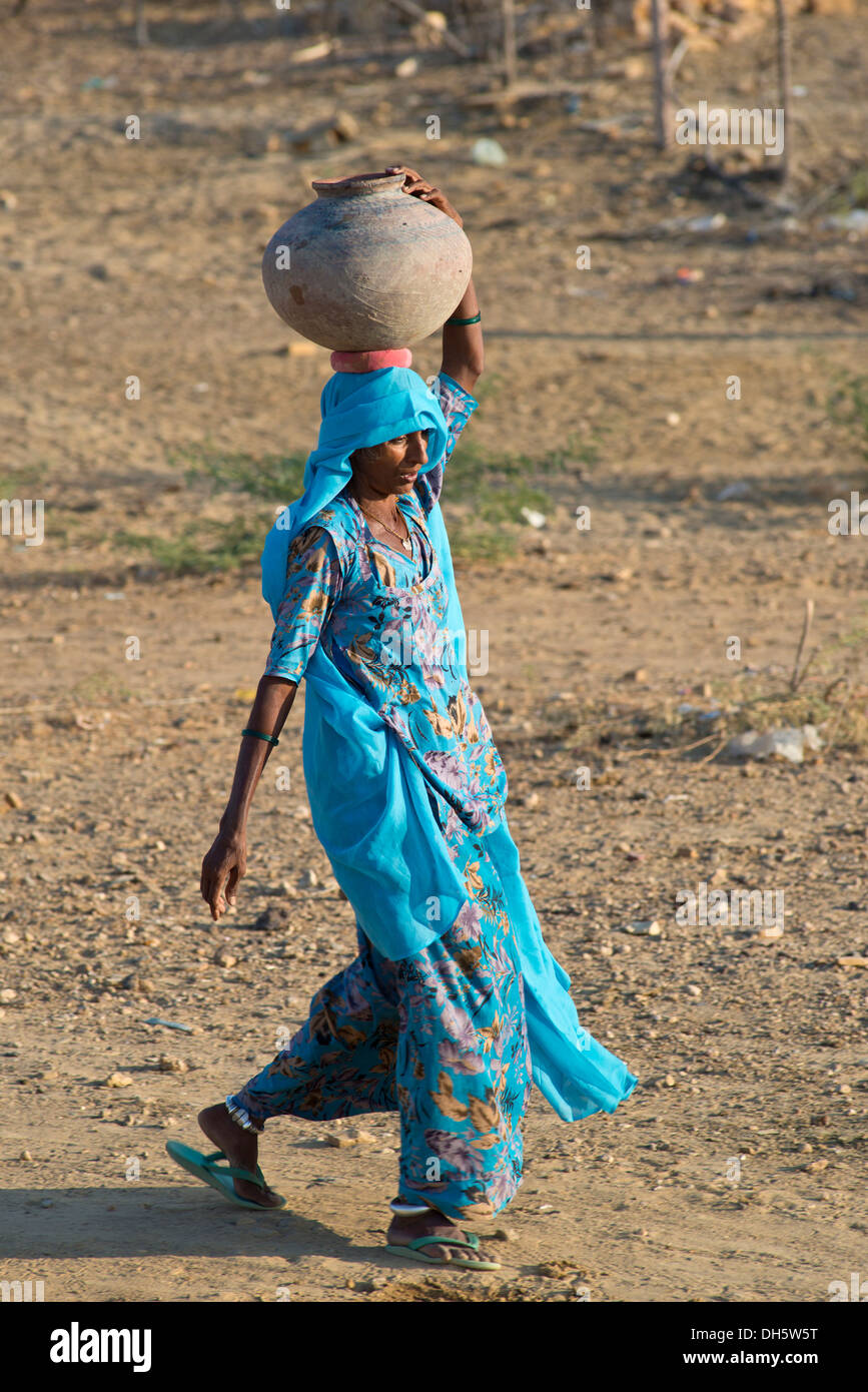 Indische Frau trägt einen leichte blaue Sari tragen einen Ton Wasserkrug auf dem Kopf, Khuri, Rajasthan, Indien Stockfoto