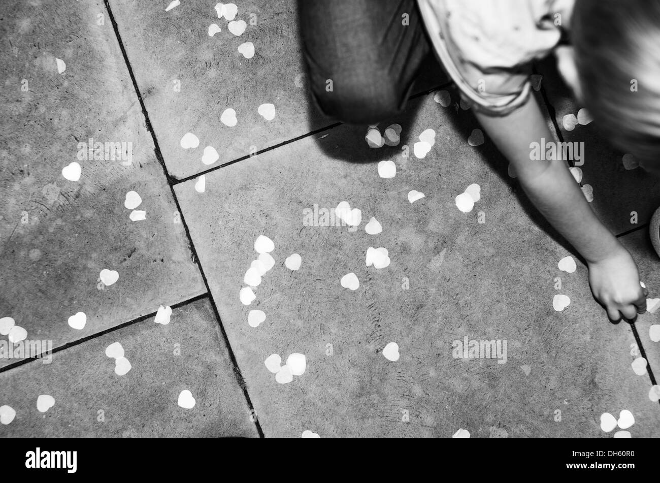Das Kind holt Konfetti für den Hochzeitsempfang vom gepflasterten Boden ab Stockfoto