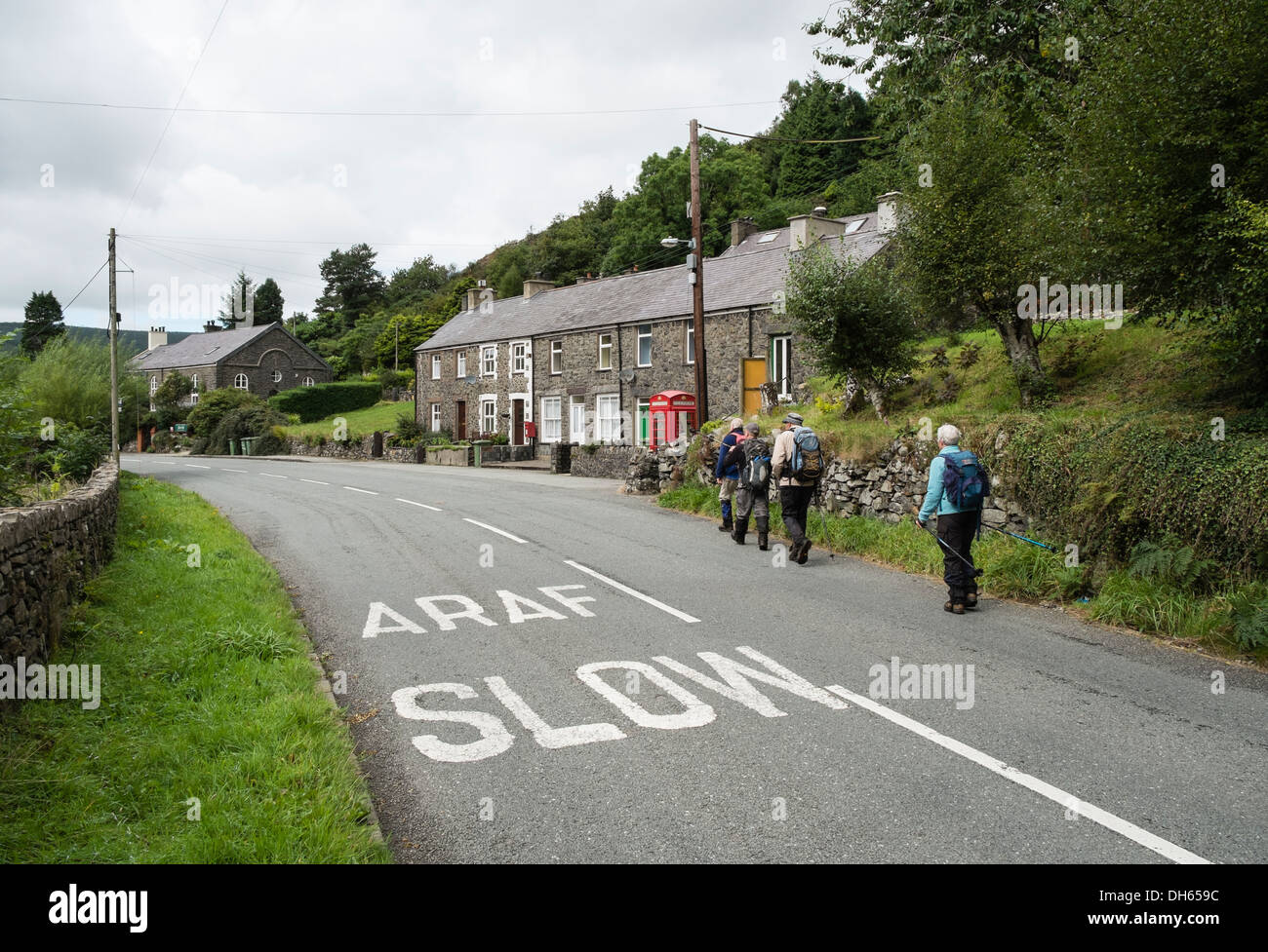 Walisisch und Englisch zweisprachige Araf Slow Zeichen gemalt an Hauptstraße mit Wanderer zu Fuß durch das Dorf. Betws Geerken Gwynedd Wales Stockfoto