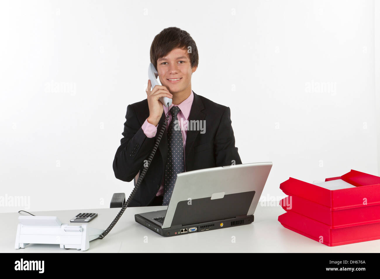 Junger Mann an einem Laptop sitzen und halten eine Telefon Stockfoto