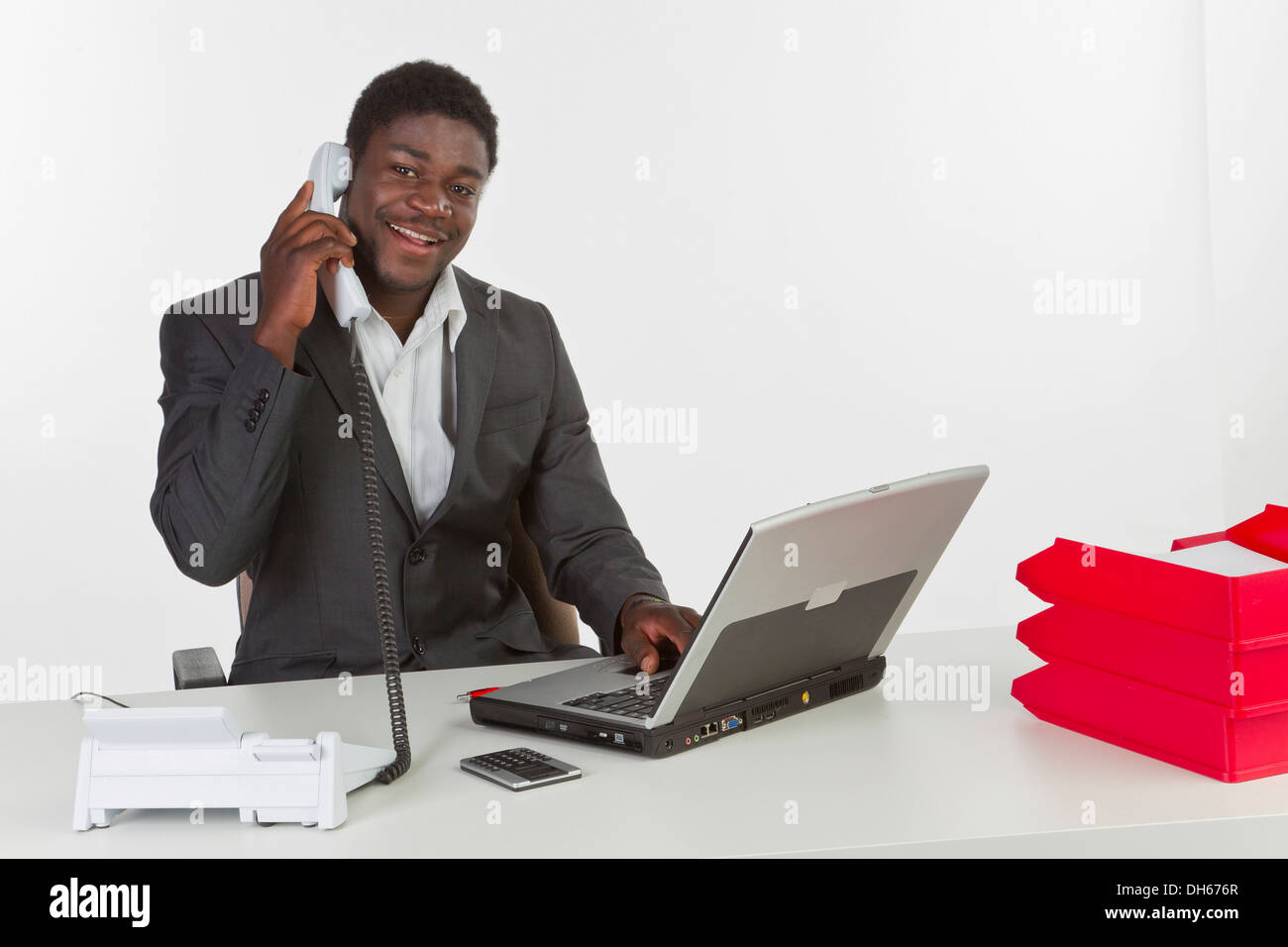Junge dunkelhäutige Mann am Laptop sitzt und hält eine Telefon Lächeln Stockfoto