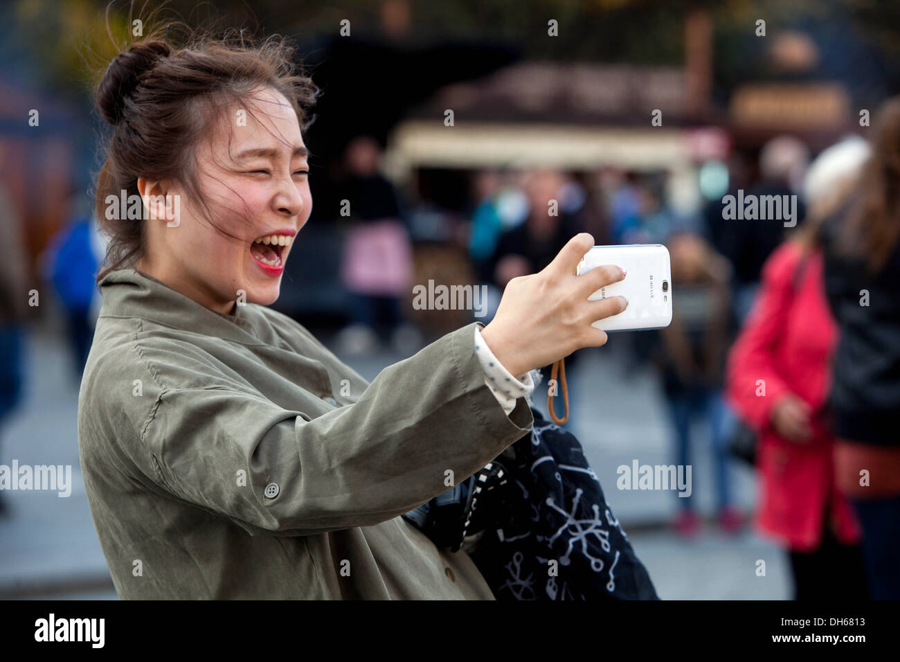 Eine asiatische Frau lächelt auf dem Altstädter Ring, Prag, Tschechische Republik. Sie lacht Menschen mit Mobiltelefonen Stockfoto