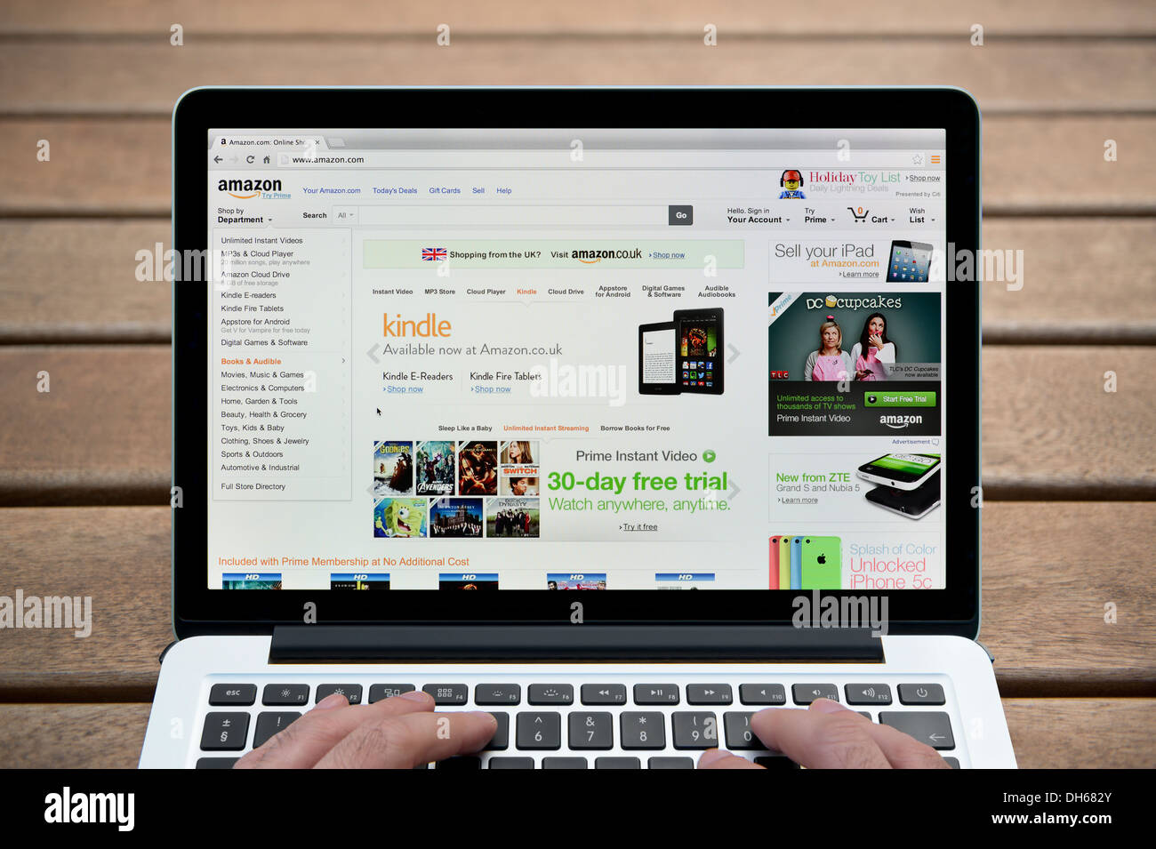 Die Amazon-Website auf einem MacBook Hintergrund eine Holzbank im Freien einschließlich eines Mannes Finger (nur zur redaktionellen Verwendung). Stockfoto
