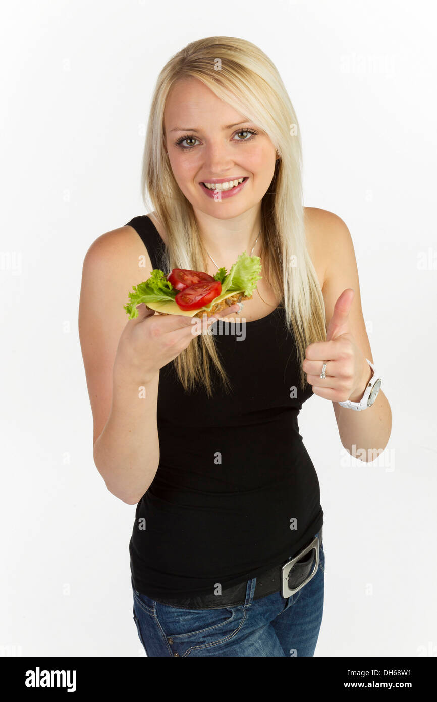 Junge Frau hält eine Scheibe Brot mit Körnern, garniert mit Tomaten und Käse Stockfoto