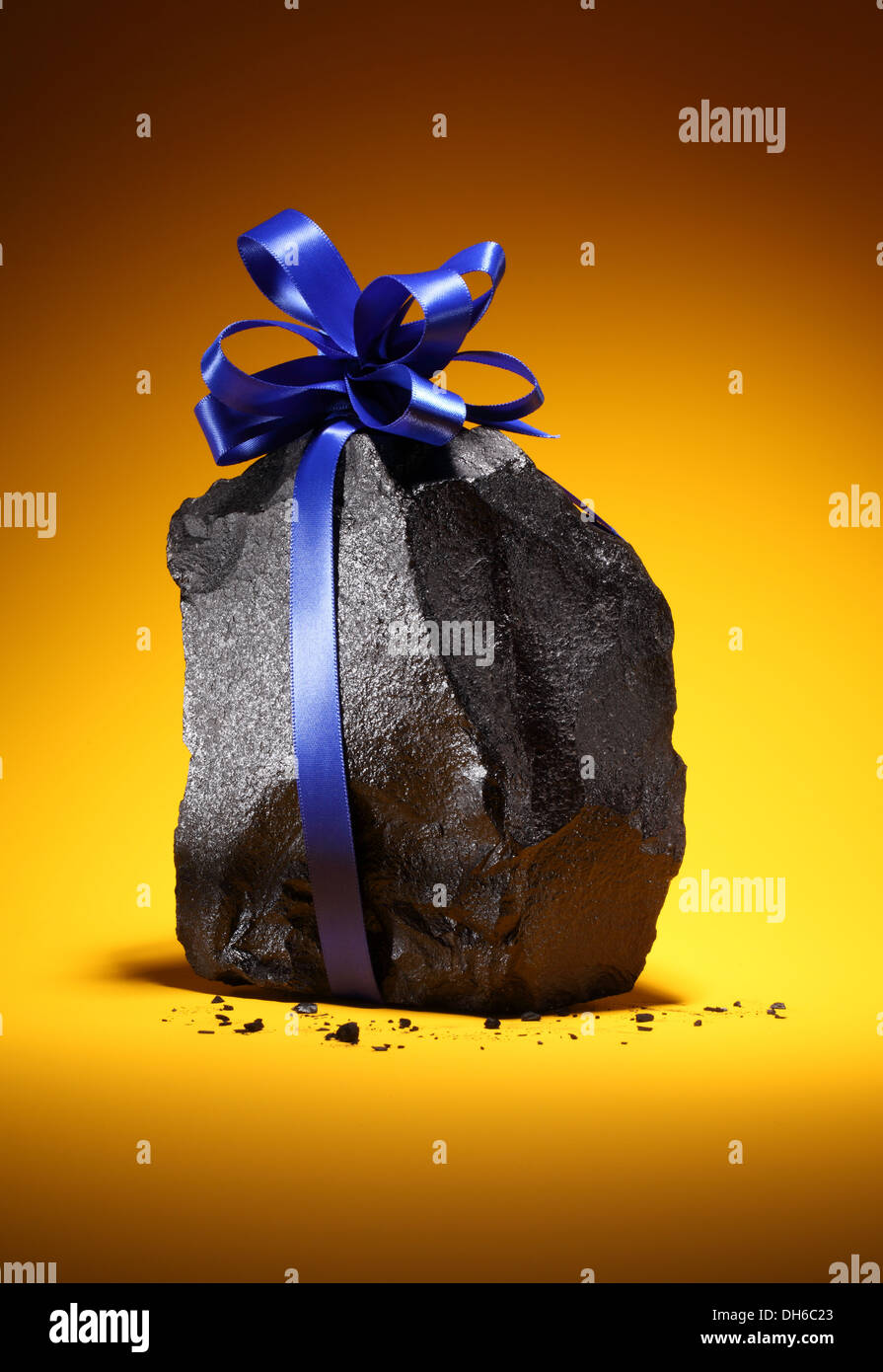 Ein schwarzen schwarzen Klumpen Kohle mit einem blauen Band gebunden um ihn herum. Leuchtend orange Hintergrund. Stockfoto