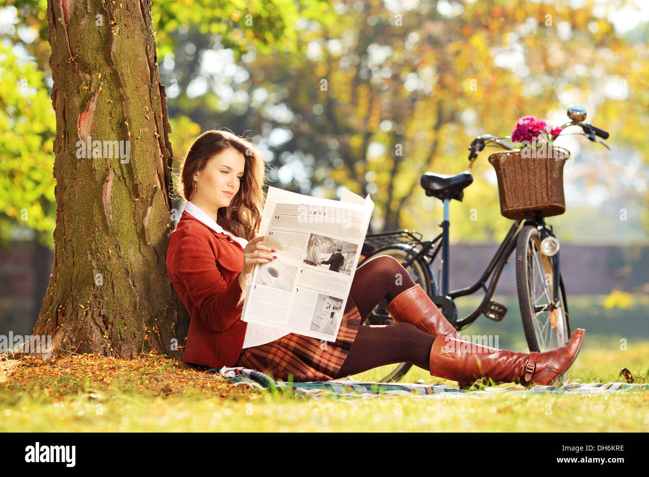 Junge Frau mit dem Fahrrad auf einer Wiese sitzen und lesen eine Zeitung in einem park Stockfoto