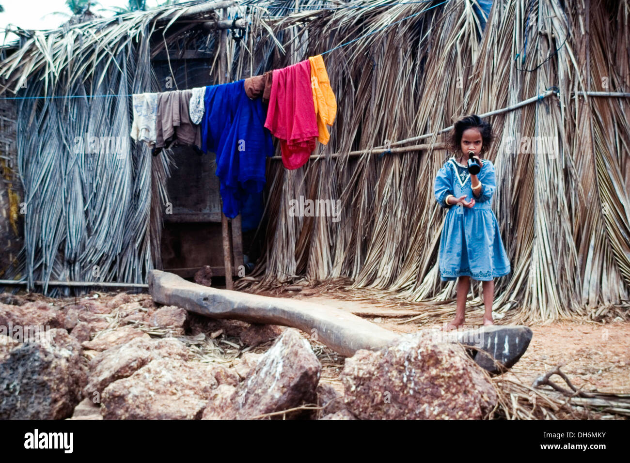 junge Mädchen trinken aus der Flasche vor ihrer Familie Stroh gebaut Hause Benaulim Goa Indien Stockfoto