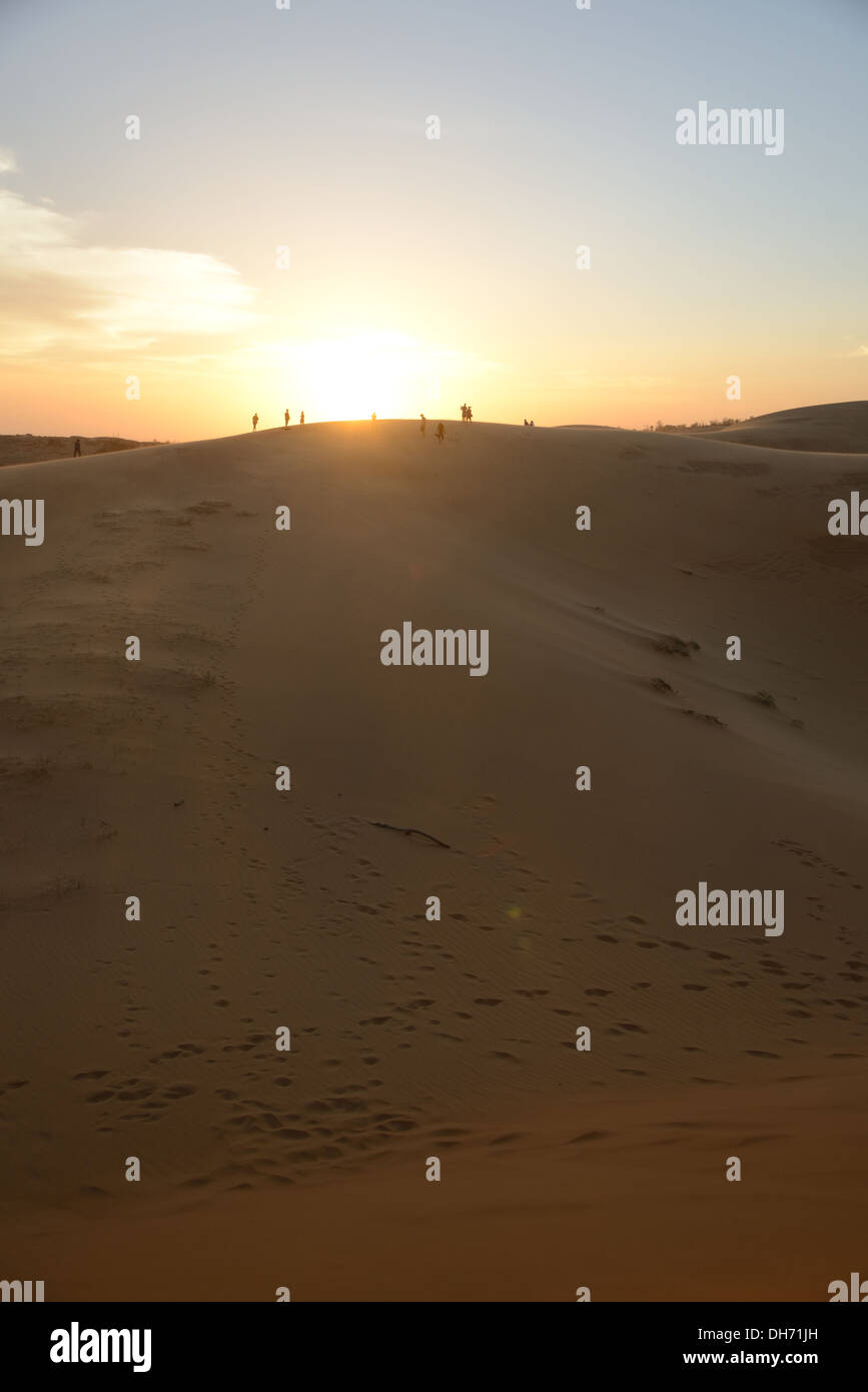 Gruppe von Menschen in der Wüste den Sonnenuntergang beobachten.  Menschen befinden sich im Abstand auf große Sanddüne. Stockfoto