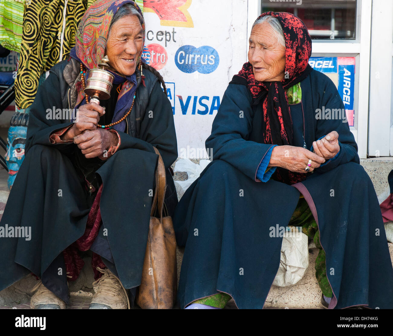 Ladakhi Frauen sitzt außerhalb ein Geschäft in Leh, auf das 21. Jahrhundert Werbebotschaft hinter ihnen ahnungslos. ladakh, Indien Stockfoto