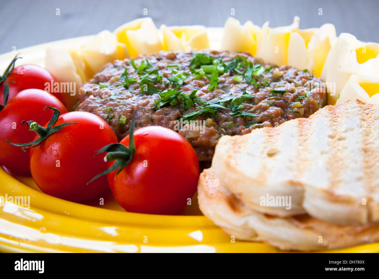 Steak Tartar mit geröstetem Brot, Tomaten und Butter auf gelbes Schild Stockfoto