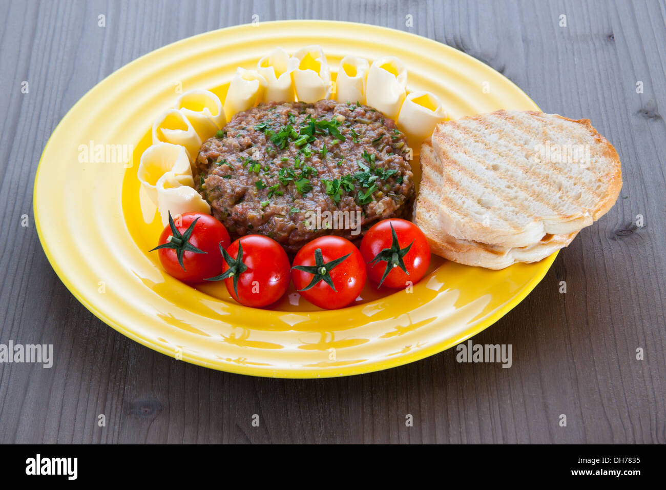 Steak Tartar mit geröstetem Brot, Tomaten und Butter auf gelbes Schild Stockfoto