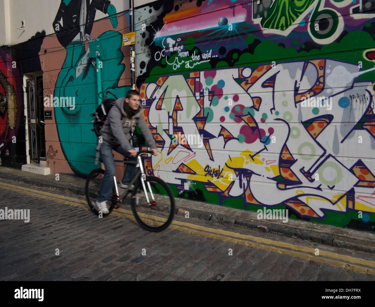 Mann-Zyklen vorbei an Graffiti auf den Straßen in der Nähe von Brick Lane, East London, UK Stockfoto