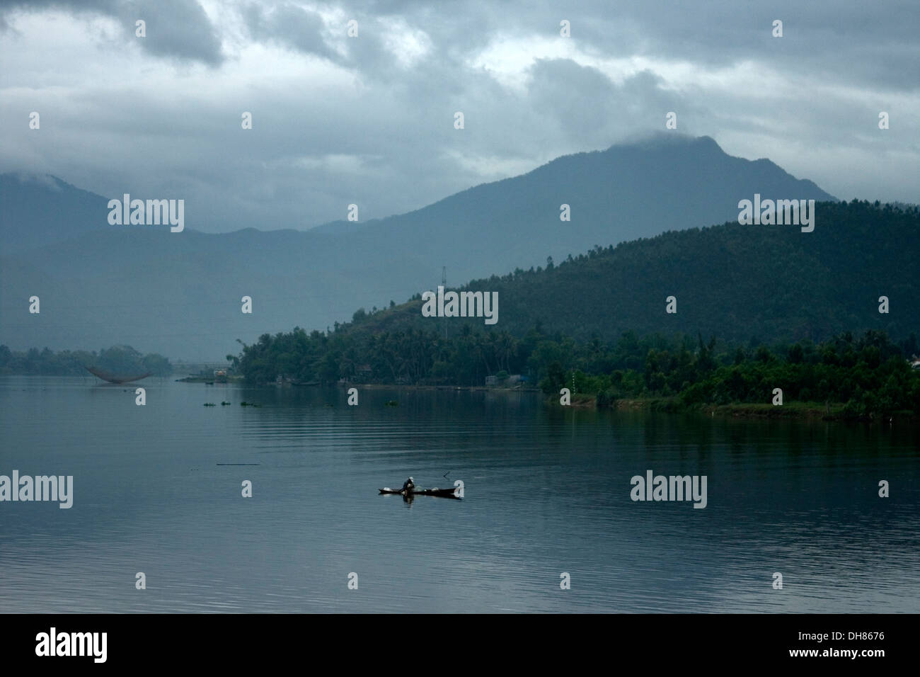 Fischer in seinem Kanu vor Sonnenaufgang, Vietnam mit Seen & Bergen umgeben. Stockfoto
