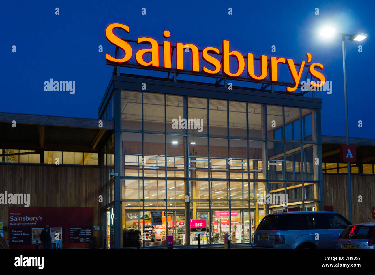 Ein großer Sainsbury Supermarkt mit dem Schild auf dem Dach leuchtet in der Nacht. Stockfoto