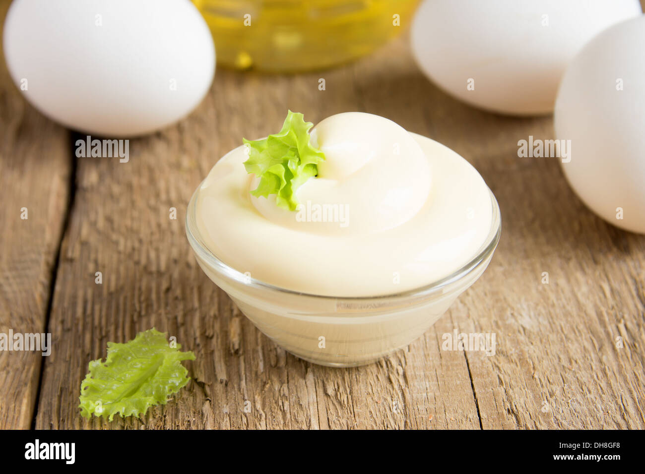Frische leckere Mayonnaise-Sauce in Schüssel mit Zutaten (Eiern, Olivenöl) auf rustikalen hölzernen Hintergrund, Nahaufnahme, horizontale Stockfoto