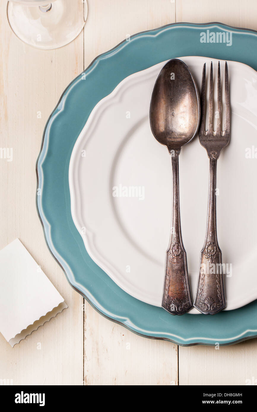 Draufsicht auf die Tischdekoration mit Vintage Besteck auf weiß und Türkis Platten mit leeren Gästekarte auf weißer Holztisch Stockfoto