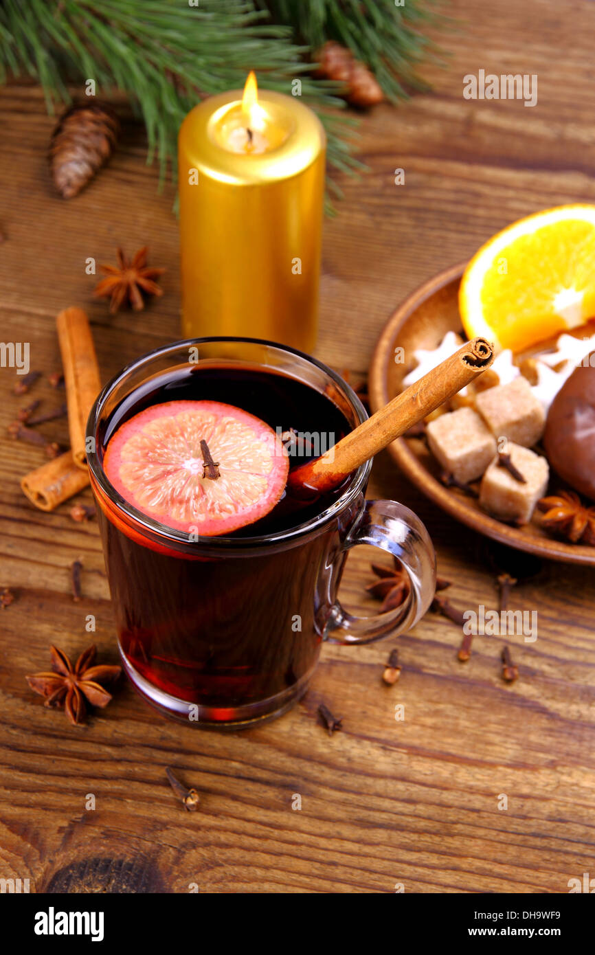 Glühwein in Glas mit Zimtstange, Kerze und Süßigkeiten, vertikale Stockfoto