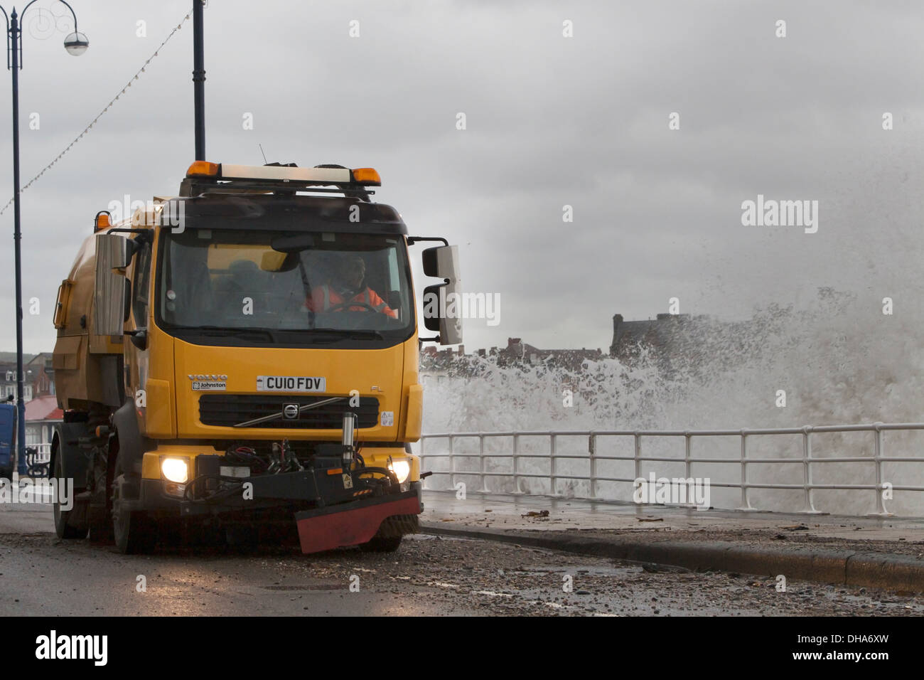 Straßenkehrer beginnt die Aufräumarbeiten nach dem Sturm in Aberystwyth mit Wellen noch Misshandlung der Küste. Stockfoto