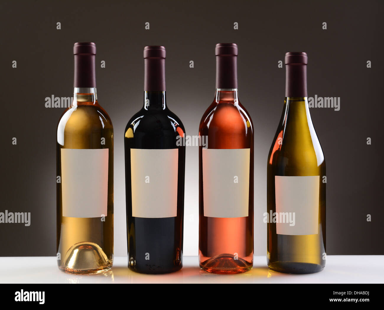 Vier Weinflaschen mit leeren Etiketten auf ein Licht, dunkelgrauen Hintergrund. Stockfoto