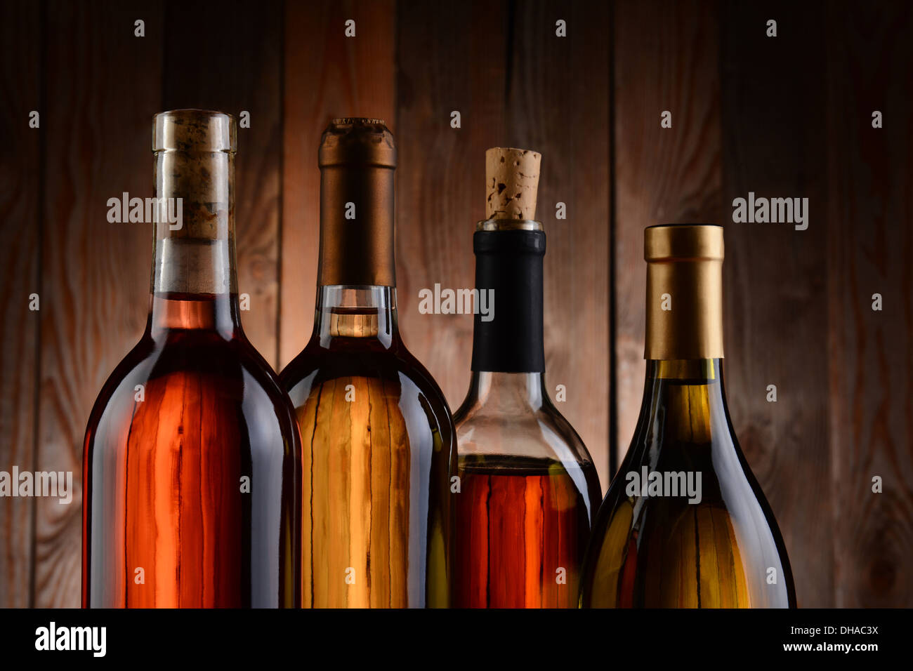 Vier Flaschen Wein, Holz im Hintergrund. Die Flaschen haben kein Label und die Textur der Hintergrund durchscheint. Stockfoto