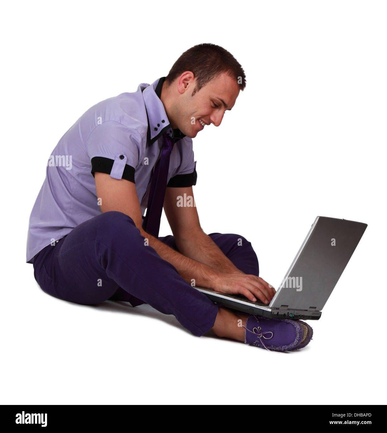 Junger Mann sitzt und arbeitet an seinem Laptop an den Füßen, vor einem weißen Hintergrund isoliert. Stockfoto