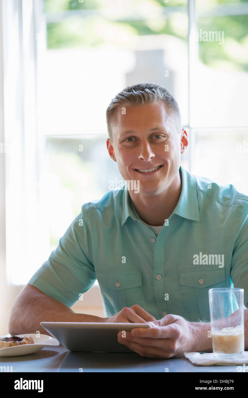 Ein Mann mit kurzen abgeschnittenen Haaren an einem Cafétisch sitzen. Mit Hilfe einer digitalen-Tablets. Stockfoto