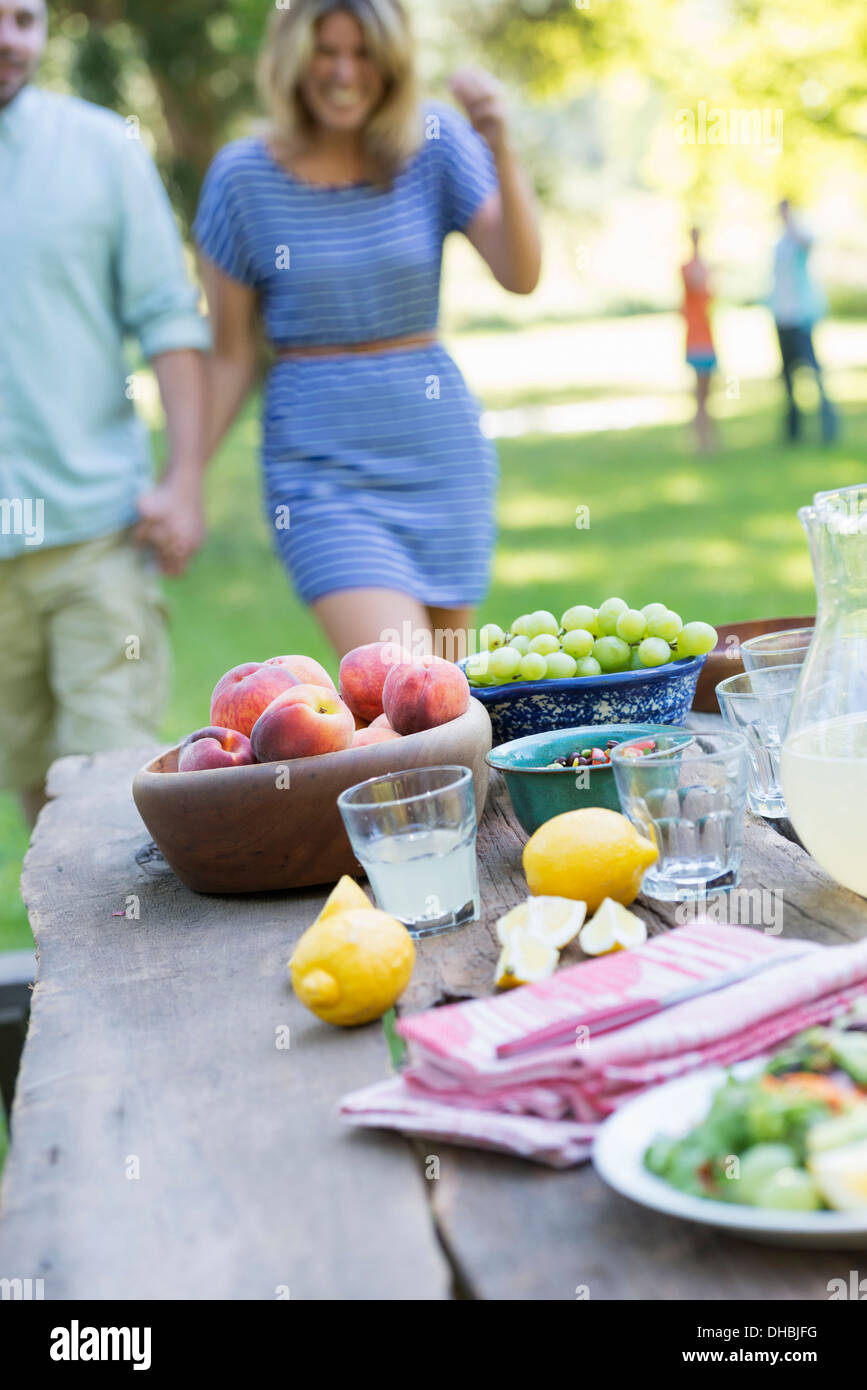 Ein Sommer-Buffet von Obst und Gemüse, auf einen Tisch gelegt. Menschen im Hintergrund. Stockfoto
